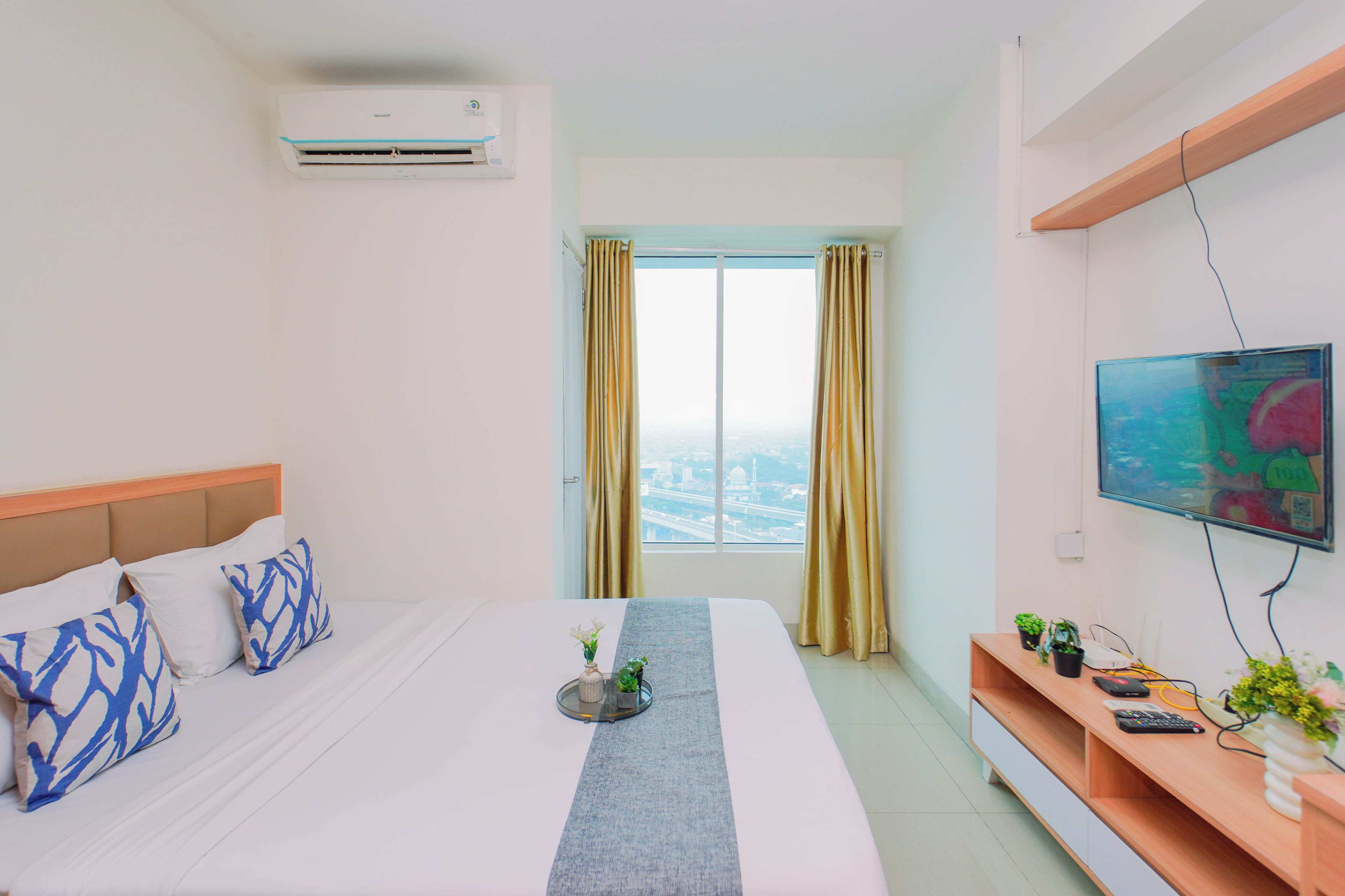Una habitación de hotel con cama, televisor, ventana con cortinas y aire acondicionado de pared.