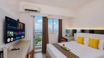 A hotel room with a large bed, a desk, a TV mounted on the wall, and a view of the city through the window.