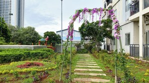 A garden pathway with stepping stones, surrounded by various plants and a purple flowering archway. - Peaceful Nest Studio At Apartment Maple Park Sunter (Jakarta)