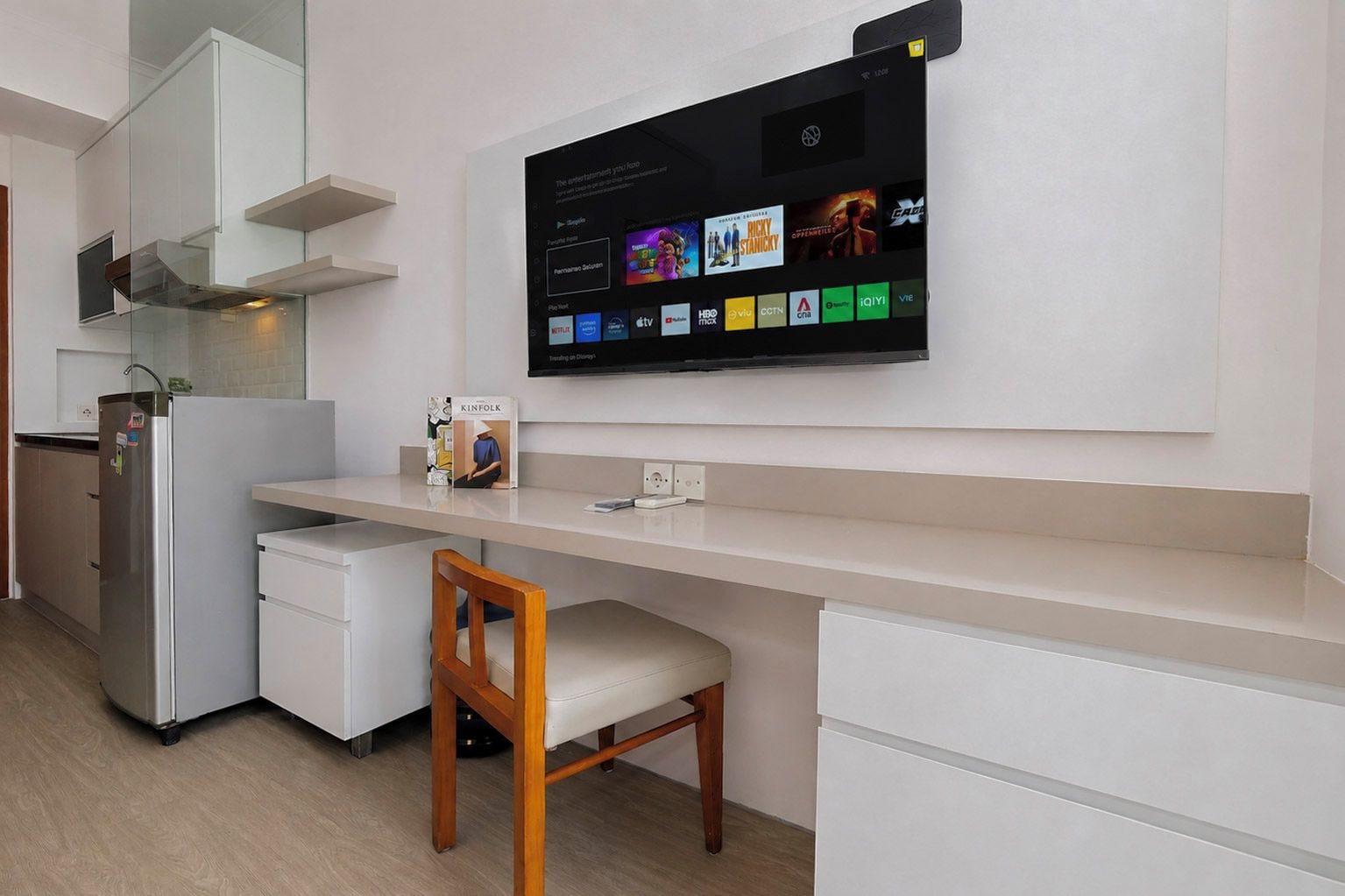 A modern kitchen with a built-in TV displaying streaming services, a refrigerator, and a wooden chair.
