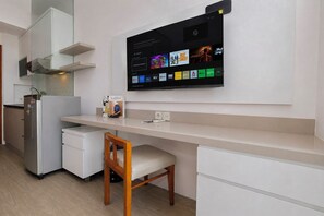A modern kitchen with a built-in TV displaying streaming services, a refrigerator, and a wooden chair. - Peaceful Nest Studio At Apartment Maple Park Sunter (Jakarta)