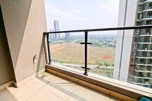 Un balcon avec une balustrade en métal, une vue sur le paysage urbain et une zone verdoyante au loin.
