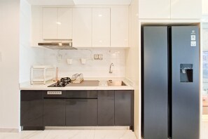 Une cuisine moderne équipée d’une cuisinière à gaz intégrée, d’un réfrigérateur en acier inoxydable et de meubles de cuisine blancs.