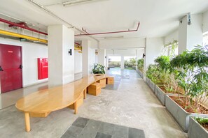 A modern indoor space with a long wooden bench, a red exit door, a fire hydrant, and potted plants along the walls. - Comfortable 2Br At Apartment Grand Kamala Lagoon (Bekasi)