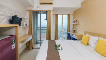 A hotel room with a bed, desk, chair, and a view of the city through large windows.