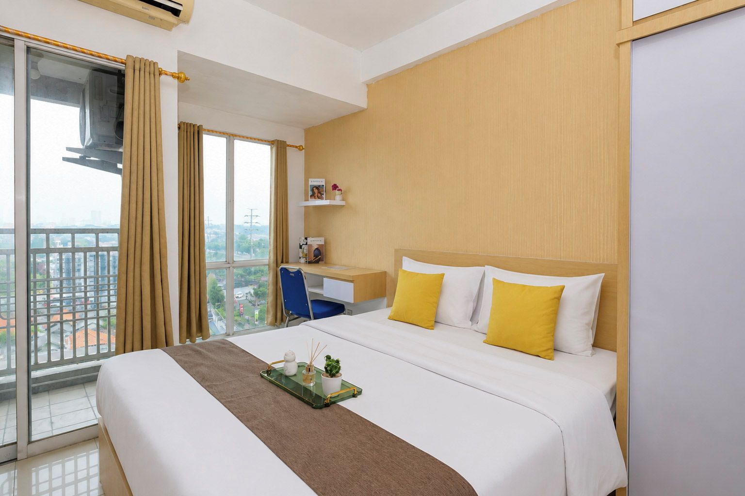 Ein Hotelzimmer mit Bett, Schreibtisch, Stuhl und Blick auf die Stadt durch große Fenster.