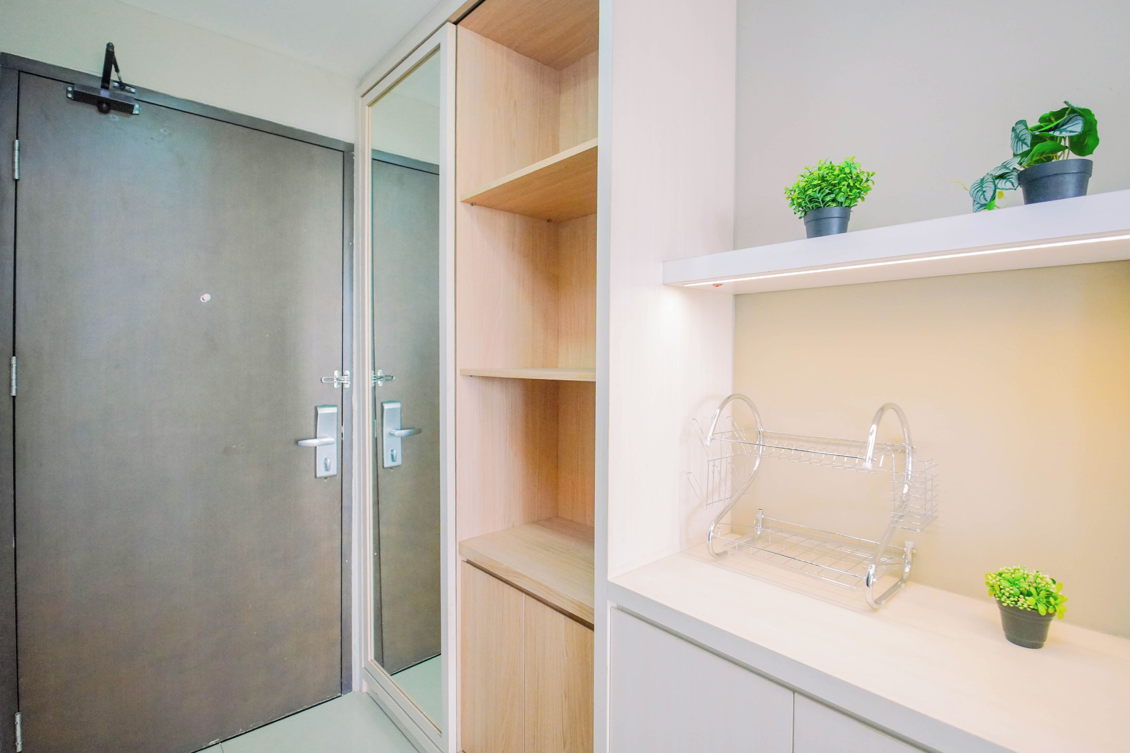 A modern bathroom with a glass shower door, a wooden vanity, and a shelf with potted plants.