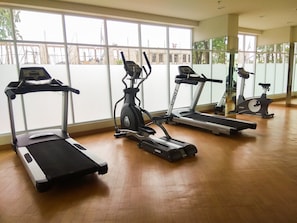 Une salle de sport équipée de quatre tapis de course, dotée de grandes fenêtres et d’un plancher en bois.