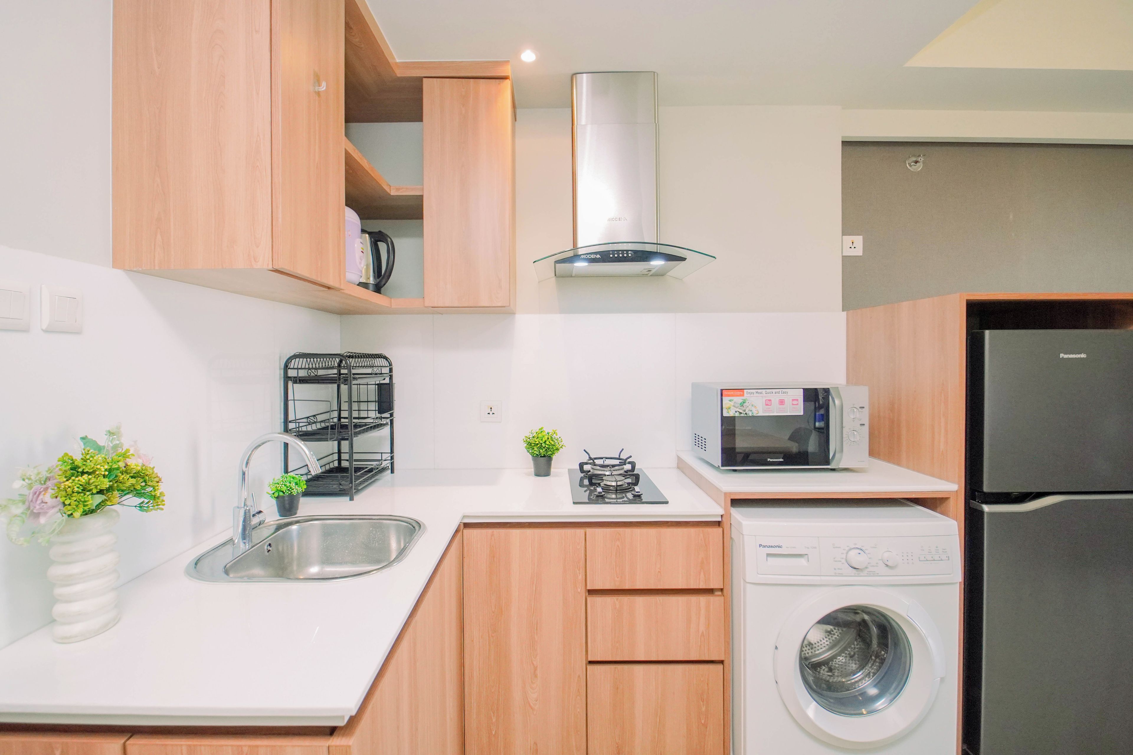 A modern kitchen with wooden cabinets, a stainless steel sink, a microwave, a refrigerator, and a washing machine.