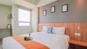 A modern hotel room with a large bed, a bedside table, a window, and a wall with framed pictures.