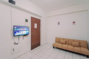 A room with a television mounted on the wall, a wooden door, a beige sofa, and a tiled floor. - Good And Homey 2Br At Apartment Kemang View (Bekasi)