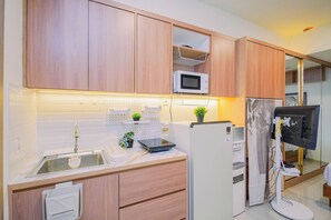 A modern kitchen with wooden cabinets, a microwave, a water dispenser, and a refrigerator. - Pleasant Warm Studio Room At Apartment Meikarta District 2 (Cikarang)