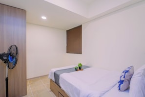 Ein Schlafzimmer mit zwei Betten, einem Standventilator, einem Fenster mit Jalousien und einer kleinen Pflanze auf dem Nachttisch.