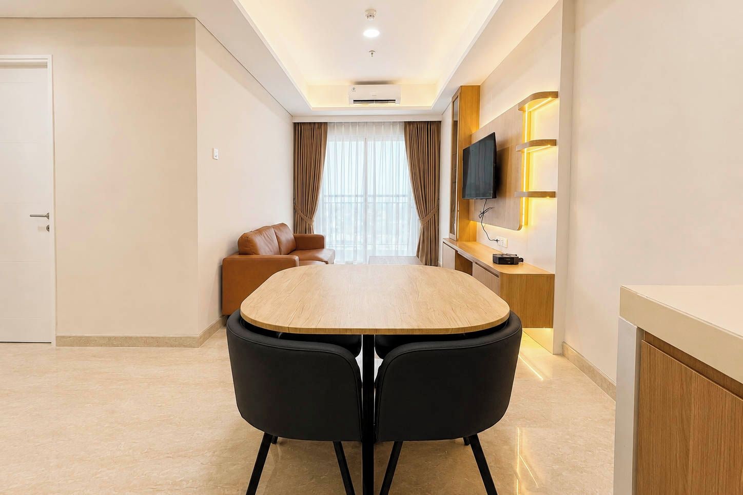 A modern hotel room with a dining table, two chairs, a sofa, a TV, and a wooden cabinet.