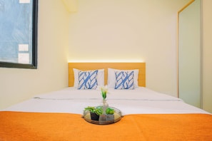 A hotel room with a bed, two pillows, a bedside table with a plant, and a window. - Bright And Modern 2Br At Apartment Meikarta District 2 (Cikarang)