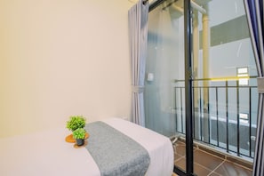A room with a bed, a small potted plant, a grey blanket, and a sliding glass door leading to a balcony. - Bright And Modern 2Br At Apartment Meikarta District 2 (Cikarang)