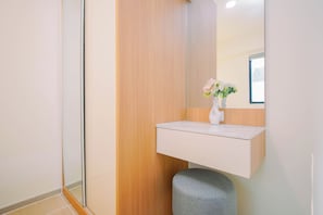 A modern bathroom with a wooden vanity, a mirror, and a vase with flowers. - Bright And Modern 2Br At Apartment Meikarta District 2 (Cikarang)