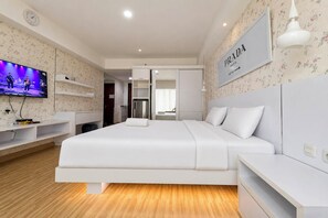 A modern hotel room with a large bed, a flat-screen TV, a minibar, and a sign indicating the location. - Fresh Living Studio At Apartment Mataram City (Yogyakarta)