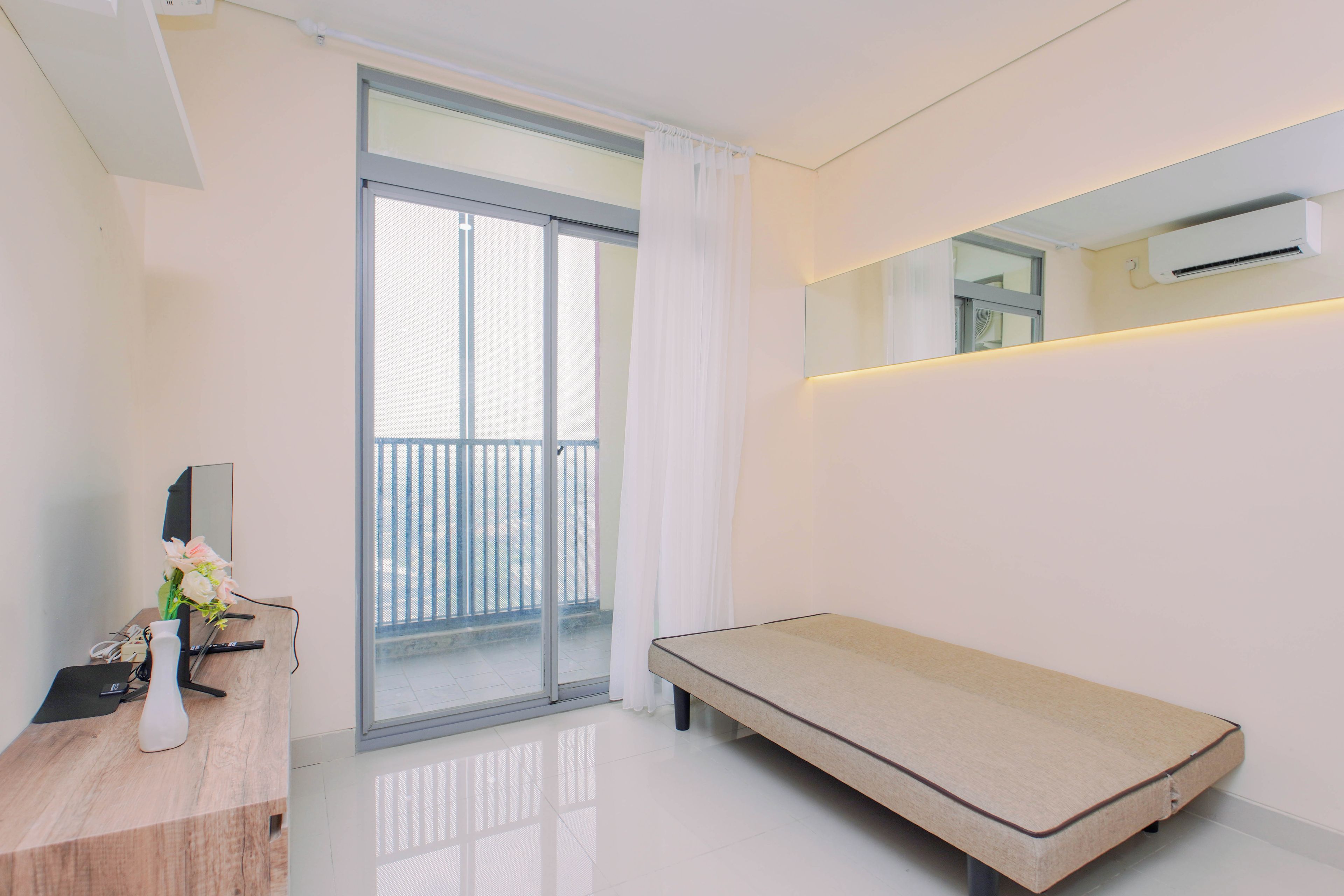 A modern bedroom with a sliding glass door, a small bedside table with a vase of flowers, a bed, and a wall-mounted air conditioning unit.
