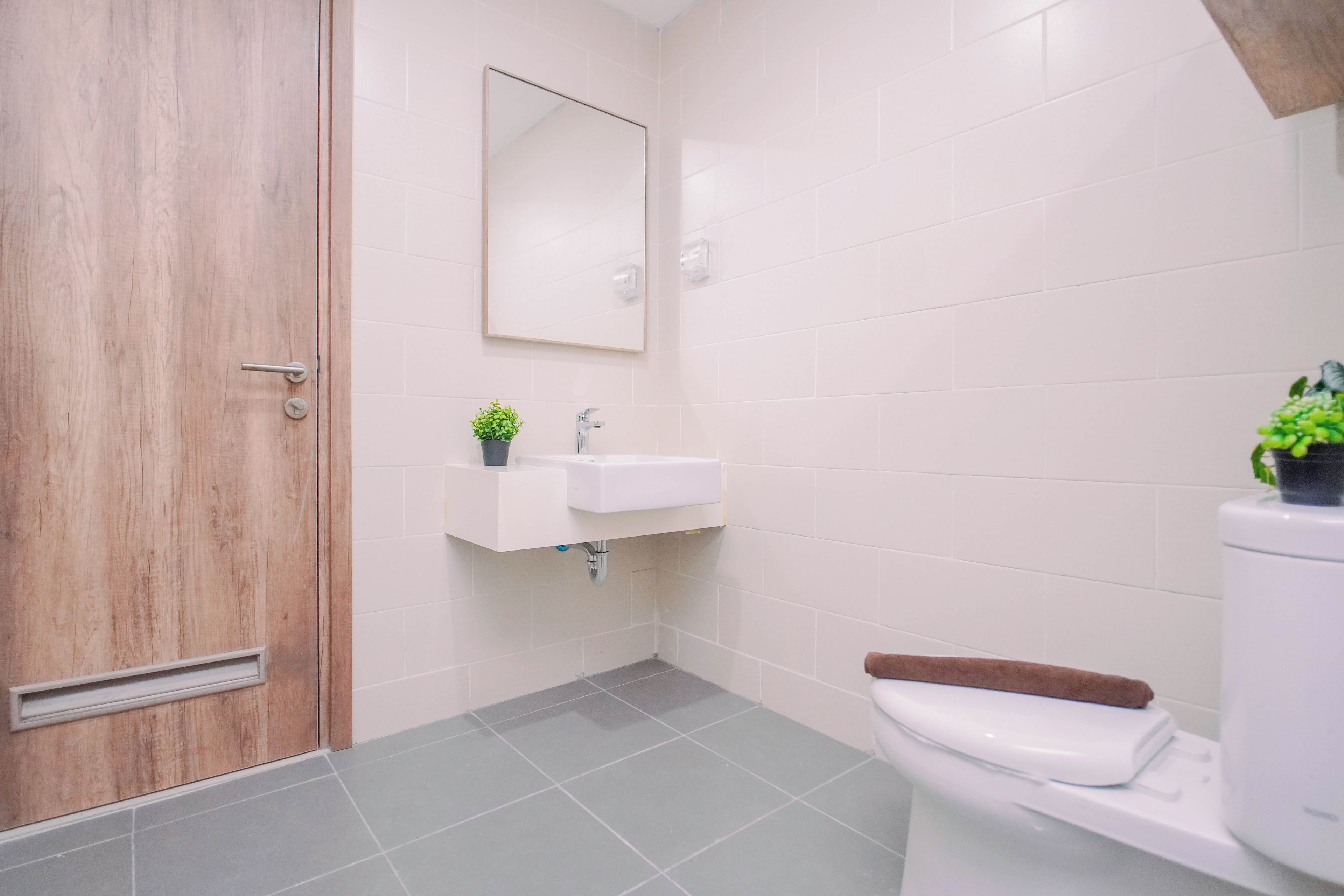 A bathroom with a wooden door, a white sink with a mirror above it, and a toilet with a brown seat.