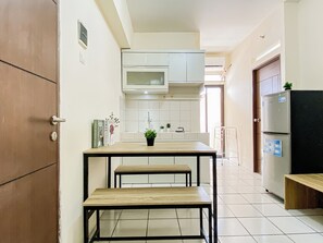 Eine Küche mit weißen Schränken, einer Mikrowelle, einem Kühlschrank und einem kleinen Tisch mit Bänken.