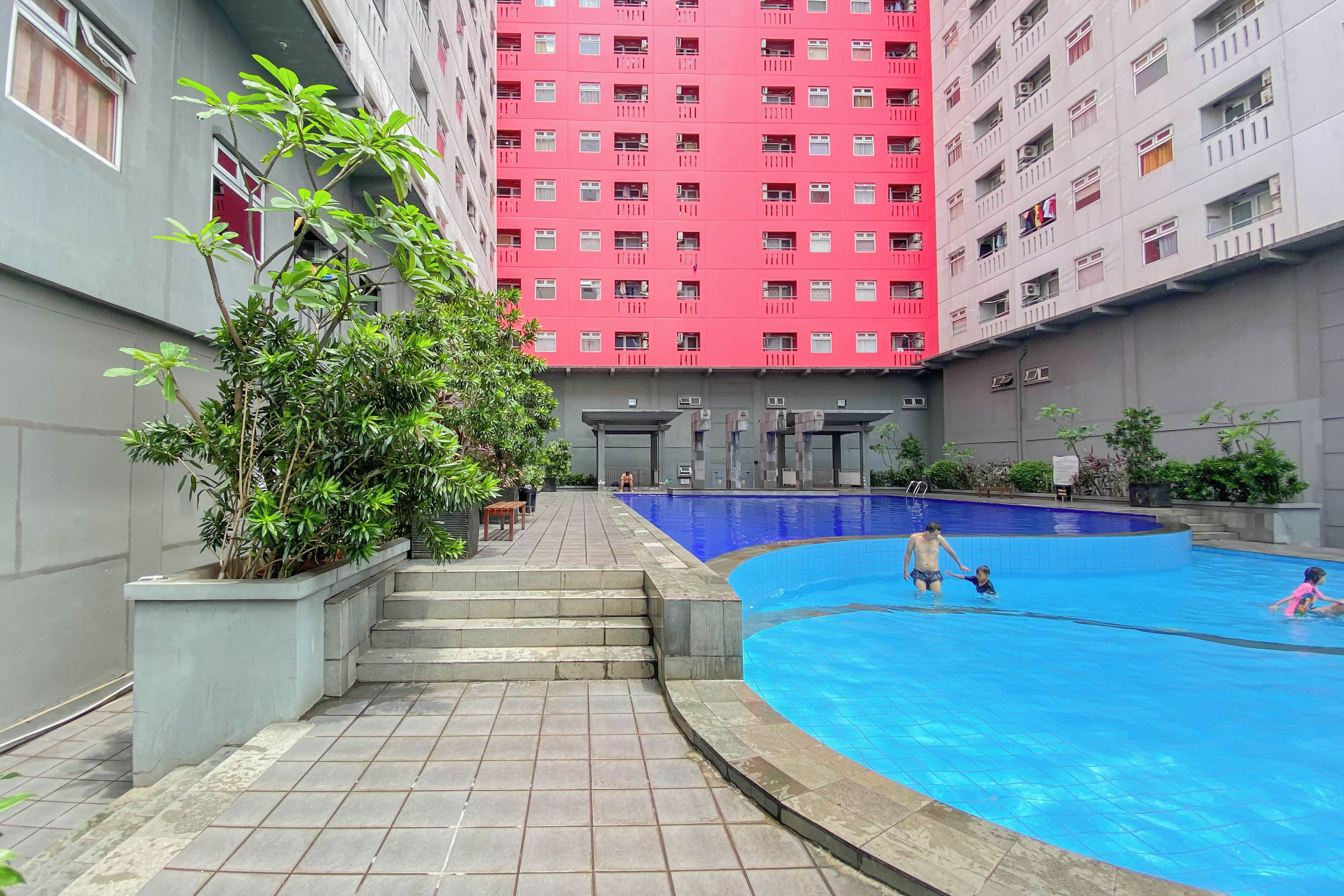 Un edificio residencial con piscina, escalones que bajan a la piscina y un edificio rojo al fondo.