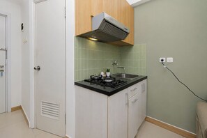 A compact kitchen with a gas stove, a built-in oven, a sink, and a ventilation hood. - Modern Minimalist 2Br At Apartment Green Pramuka City (Jakarta)