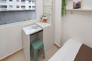 A small, clean room with a window, a desk, a green stool, a bed, and a shelf with a book. - Modern Minimalist 2Br At Apartment Green Pramuka City (Jakarta)