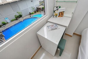 A room with a view of a swimming pool, a window, and a desk with a newspaper and a book. - Modern Minimalist 2Br At Apartment Green Pramuka City (Jakarta)