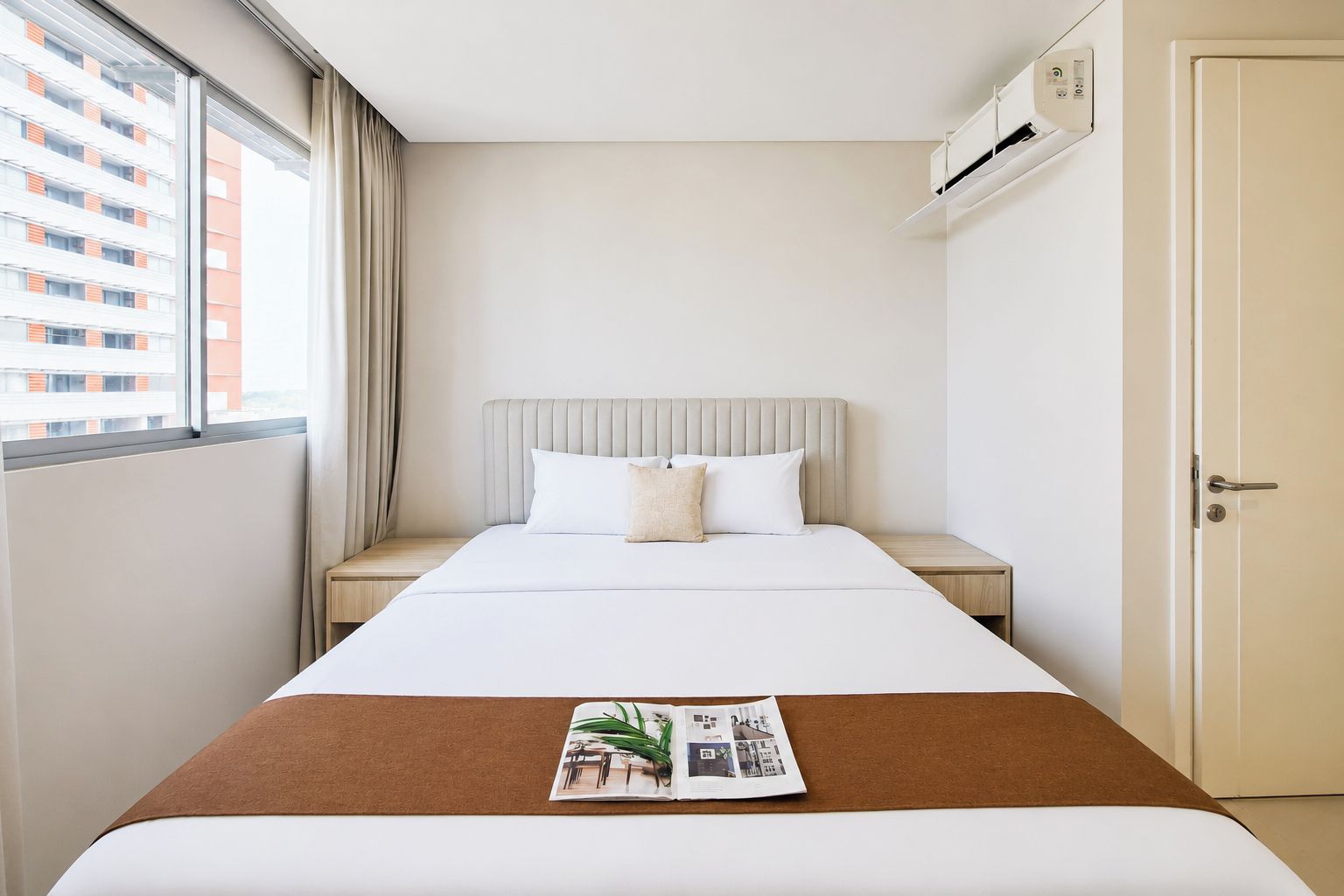 Habitación de hotel con cama, mesita de noche, ventana con cortinas, unidad de aire acondicionado y puerta.
