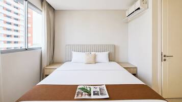 Habitación de hotel con cama, mesita de noche, ventana con cortinas, unidad de aire acondicionado y puerta.
