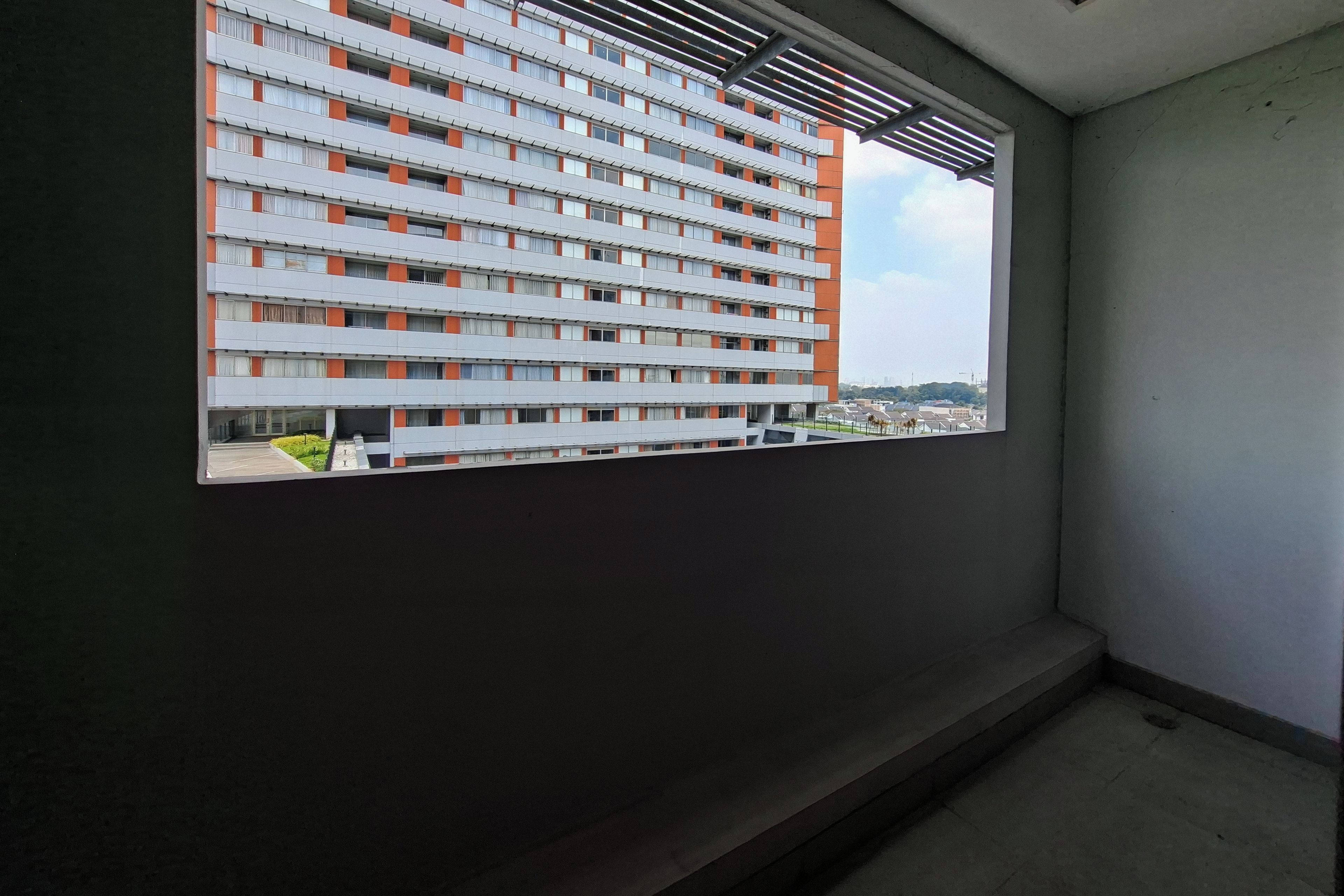 Vista a través de una ventana de un edificio de varios pisos con diseño moderno, que cuenta con una serie de balcones y un cielo despejado al fondo.