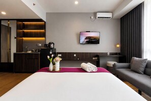 Ein Hotelzimmer mit Bett, Wandfernseher, einer Küchenzeile und einer Sitzecke mit Sofa und Sessel.