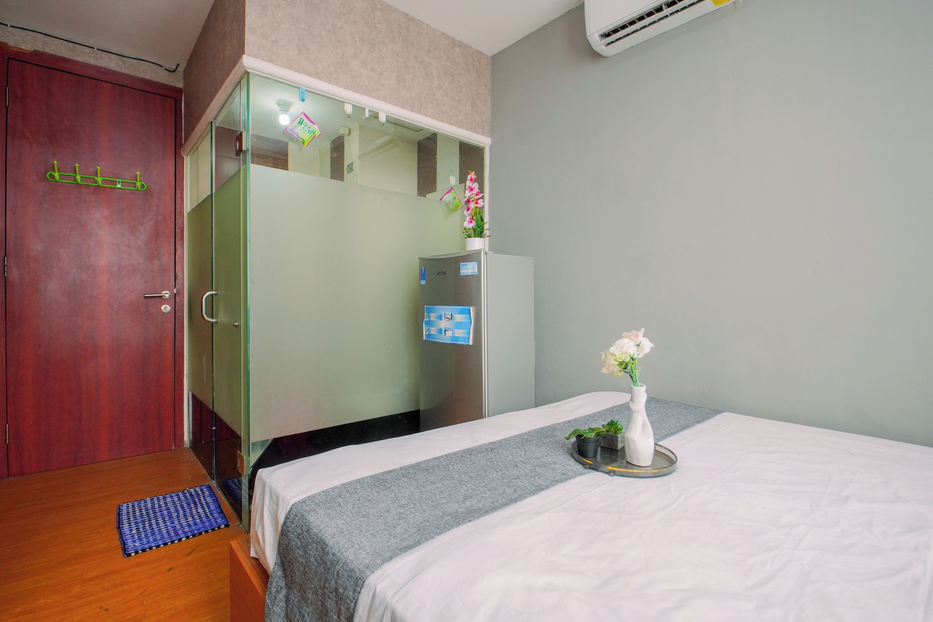 Habitación de hotel con cama, armario, espejo, una mesita con un florero y una puerta con un perchero verde.