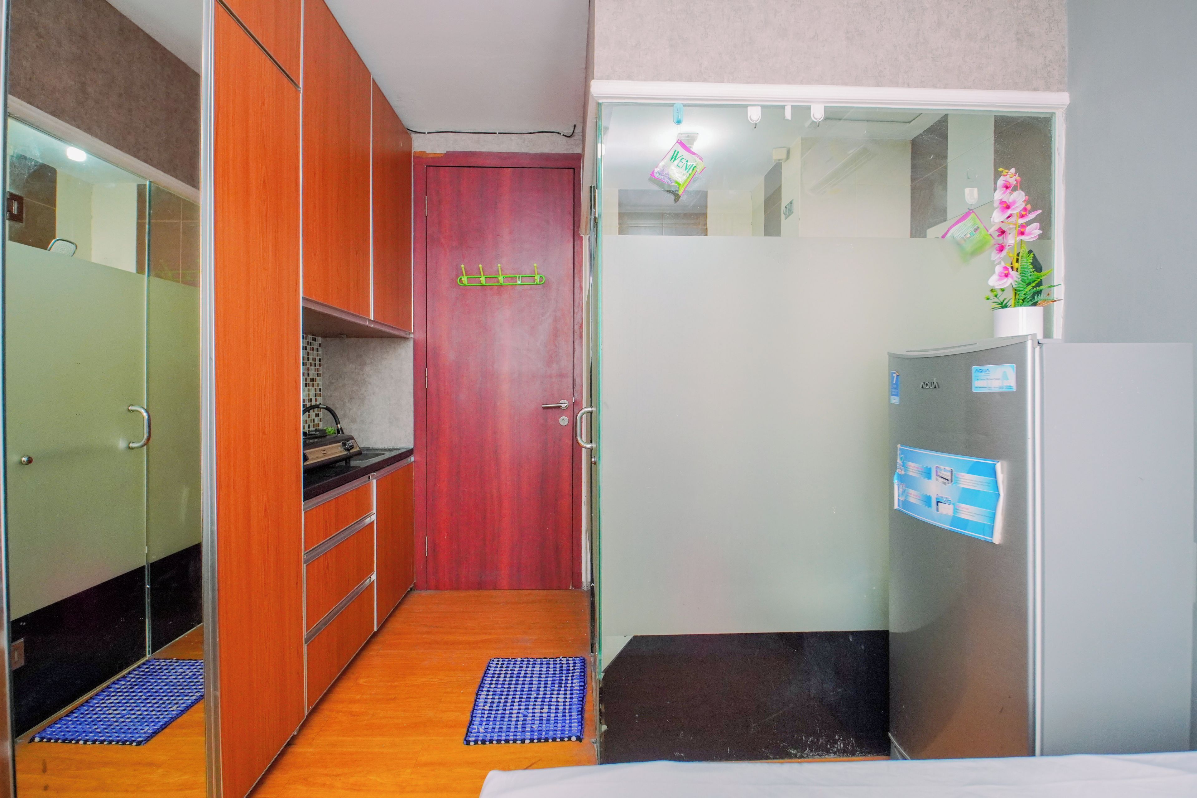 A compact hotel room with a kitchenette, a refrigerator, a bed, and a small bathroom.