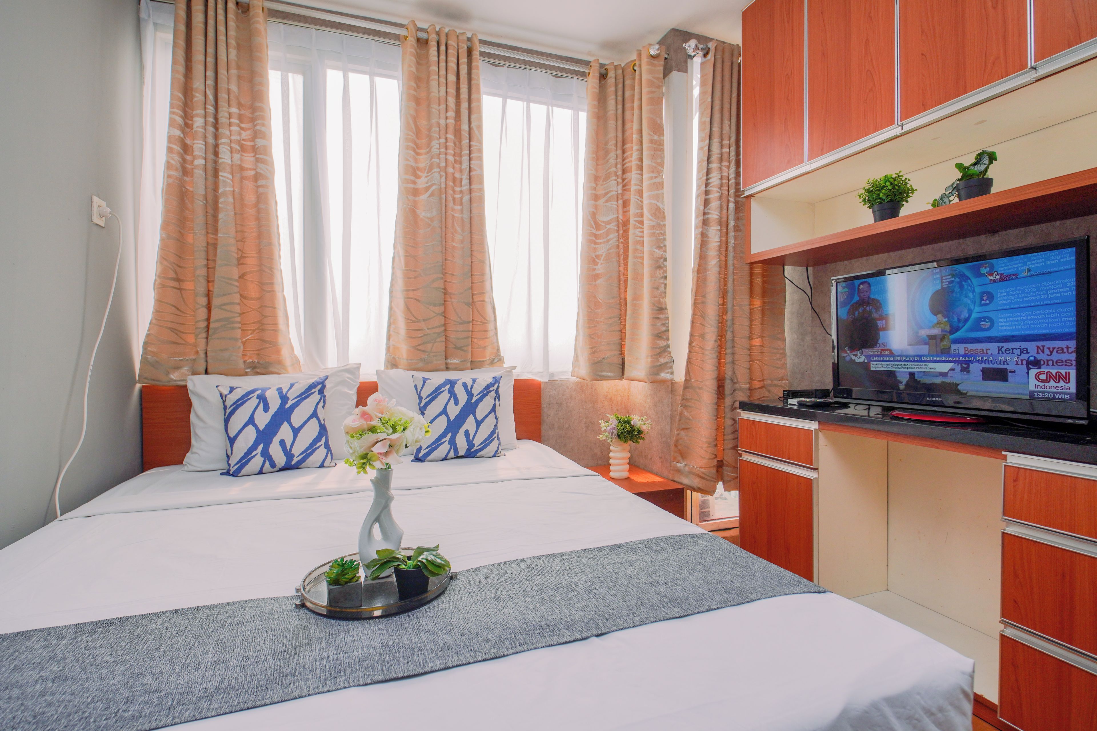 Quarto de hotel com cama, televisão e janela com cortinas.