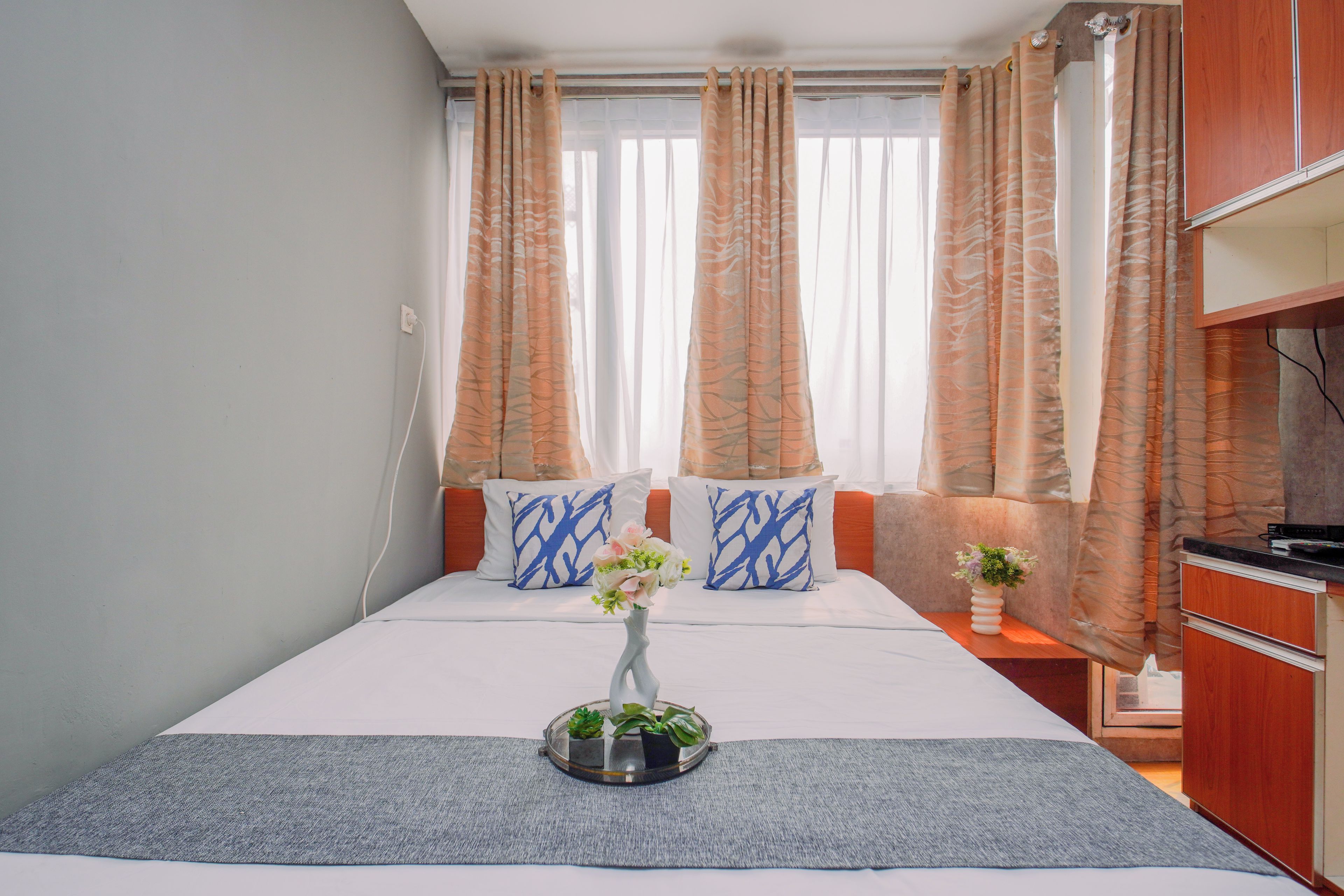 A bedroom with a bed, two pillows, a vase with flowers, a small plant, and a wooden cabinet.
