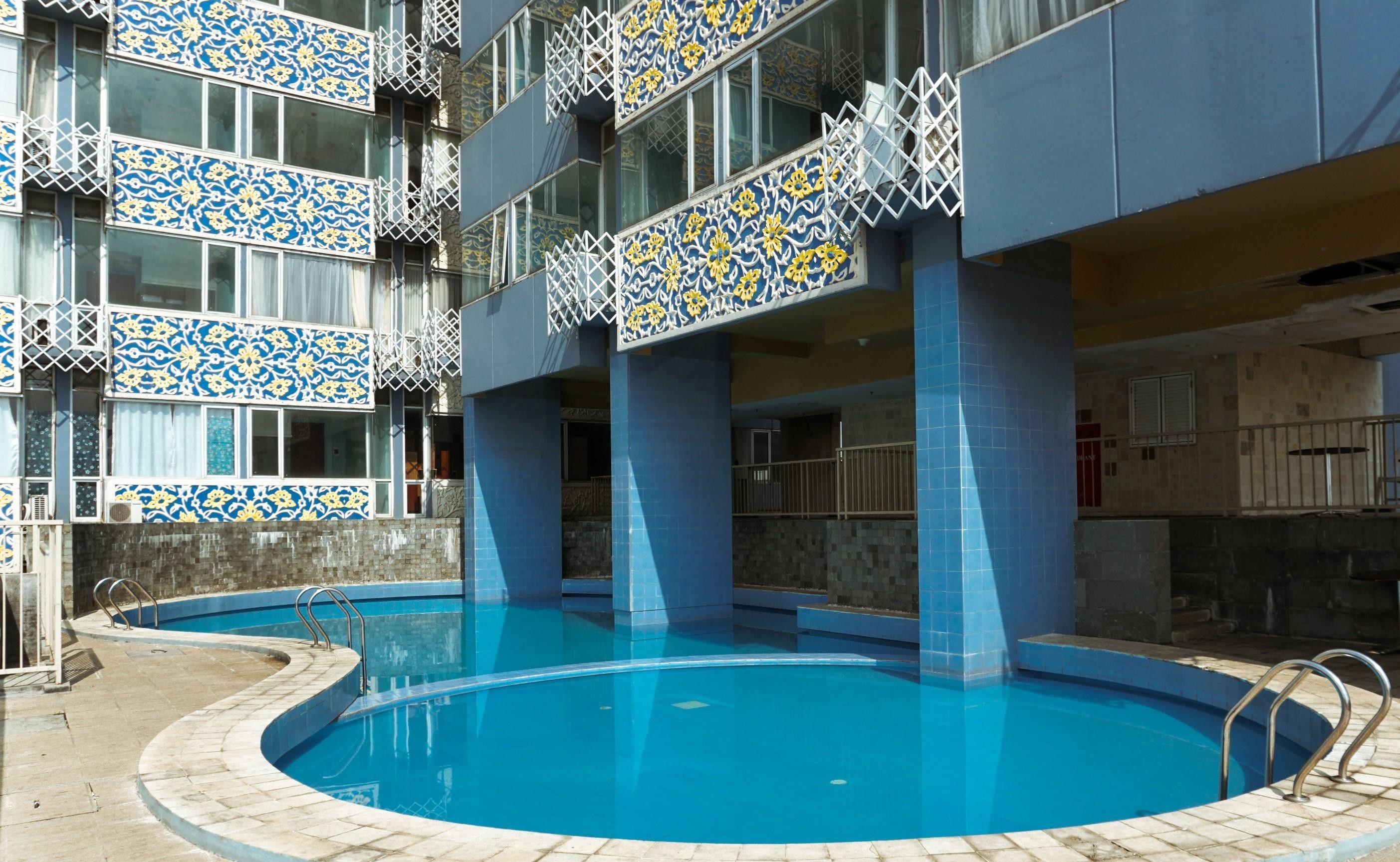 Um edifício com piscina, varandas com azulejos estampados e um céu azul límpido.