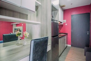 A modern kitchen with a built-in oven, a dining area with a table and chairs, and a red accent wall. - Cozy Living 1Br At Apartment Atlanta Residence (Depok)