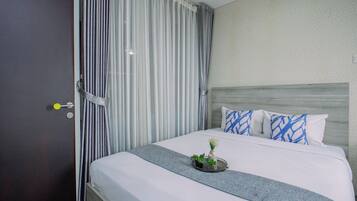 A hotel room with a bed, a nightstand, a door, and curtains.