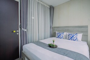 A hotel room with a bed, a nightstand, a door, and curtains. - Cozy Living 1Br At Apartment Atlanta Residence (Depok)