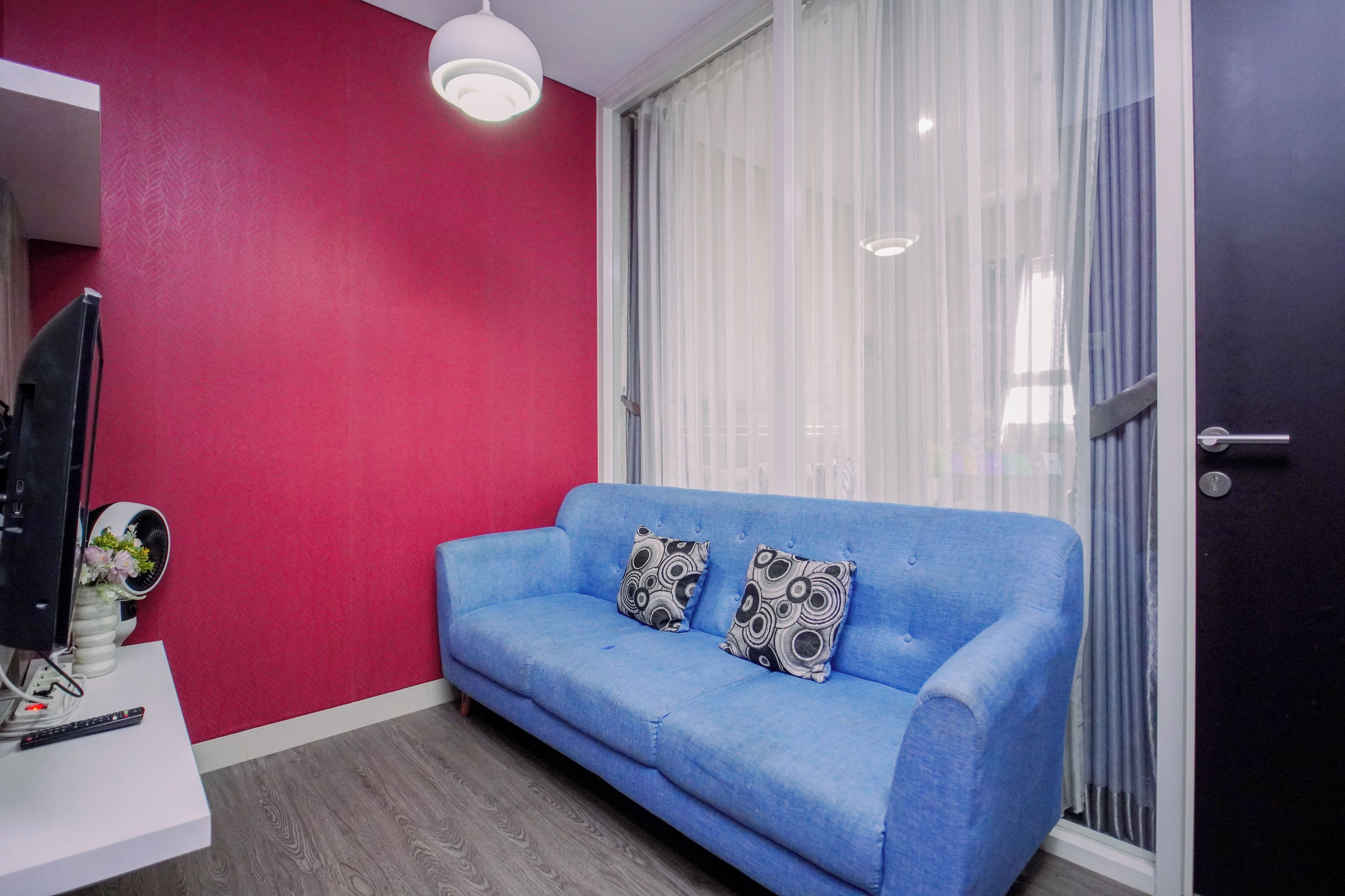 A room with a blue sofa, a white table with a remote control, and a television.
