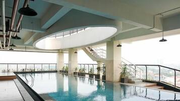 An indoor swimming pool with a view of the city, a staircase, and a modern ceiling design.