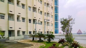 A multi-story hotel with a central courtyard, a swimming pool, and a view of a body of water. - Cozy Living 1Br At Apartment Atlanta Residence (Depok)