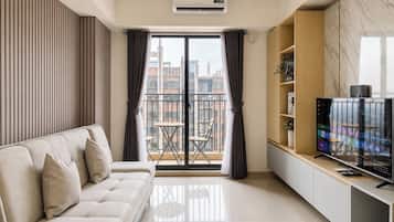 Una sala de estar moderna con un sofá, televisor y un balcón con vistas a edificios.