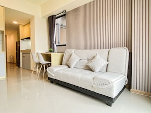 A modern living room with a sofa, a dining area, and a kitchen in the background. - Capacious And Warm 2Br At Apartment Meikarta District 1 (Cikarang)