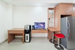 Eine kompakte Küchenzeile mit Kühlschrank, Kaffeemaschine, Computer und Fernseher, auf dem eine Sendung läuft.