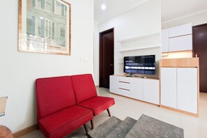 A living room with a red sofa, a TV on a white cabinet, and a framed picture on the wall. - Elegant Airy 2Br At Apartment Asatti (Tangerang)