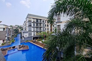 A modern multi-story residential building with a central swimming pool, surrounded by lush greenery and palm trees. - Elegant Airy 2Br At Apartment Asatti (Tangerang)