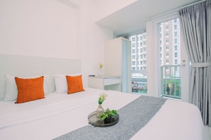 A hotel room with a large bed, white walls, and a view of a building through a window. - Efficient Studio (No Kitchen) At Apartment Tokyo Riverside Pik 2 (Jakarta)